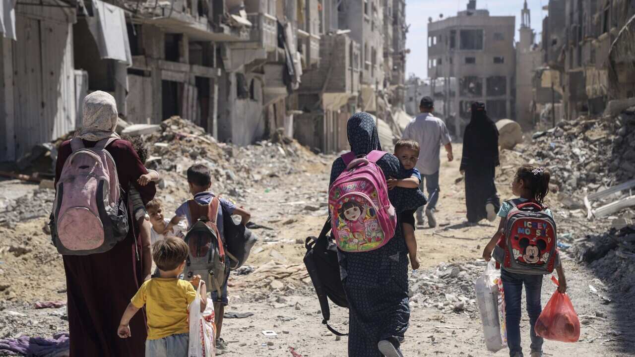 A group of Palestinian women and children walk through rubble among buidlings.