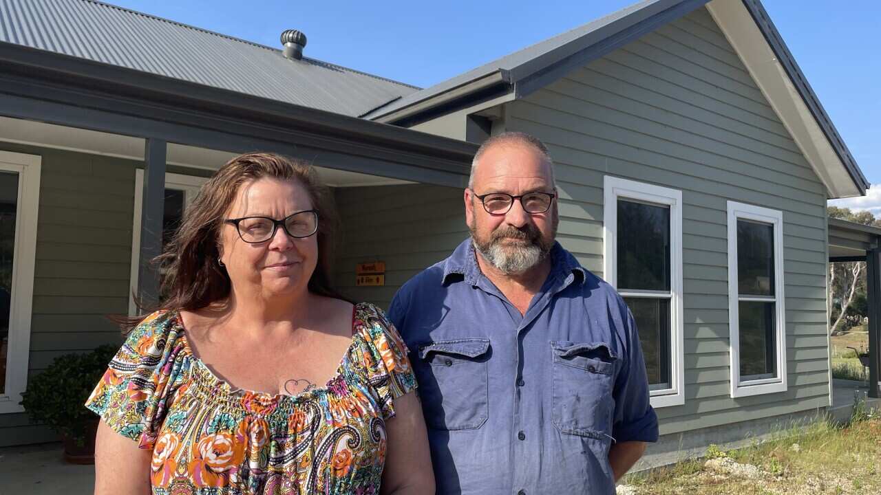 A woman and a man stand outside a house