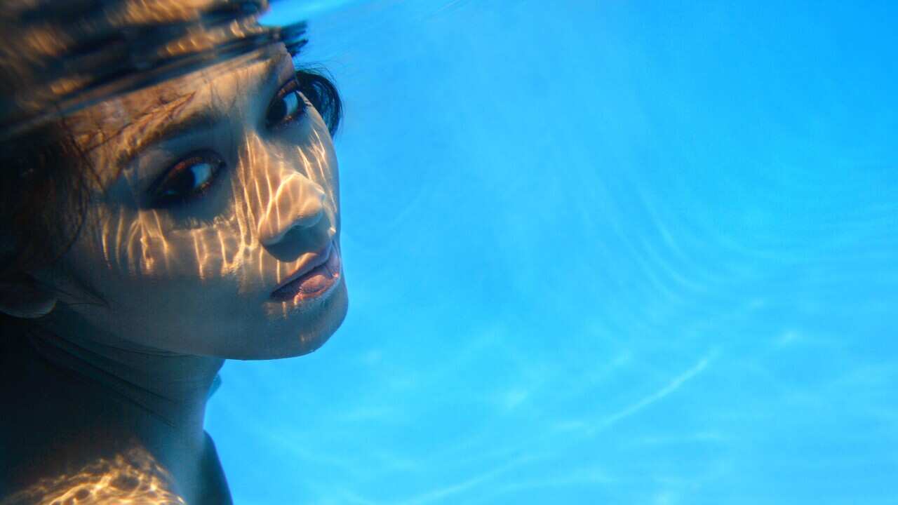 Young woman underwater looking to side at camera.