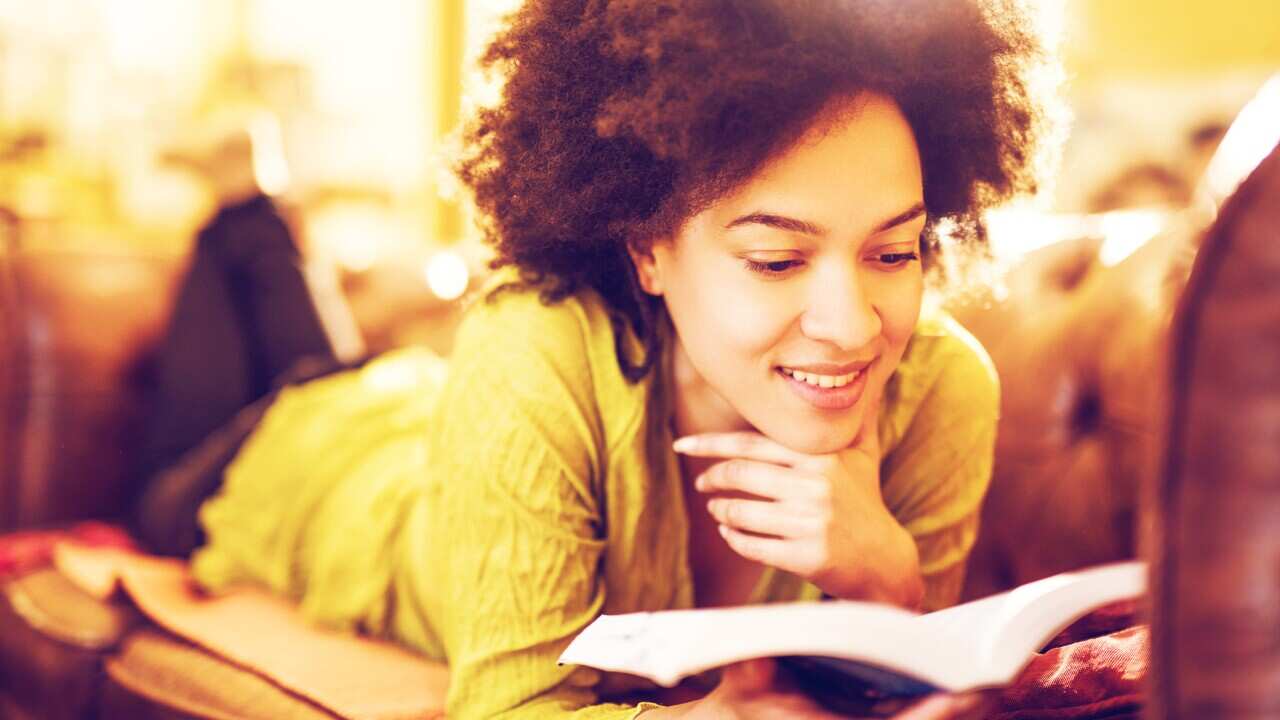 Young smiling African American student reading a book.