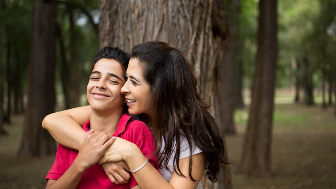 Affectionate latin mother embracing teen son and smiling