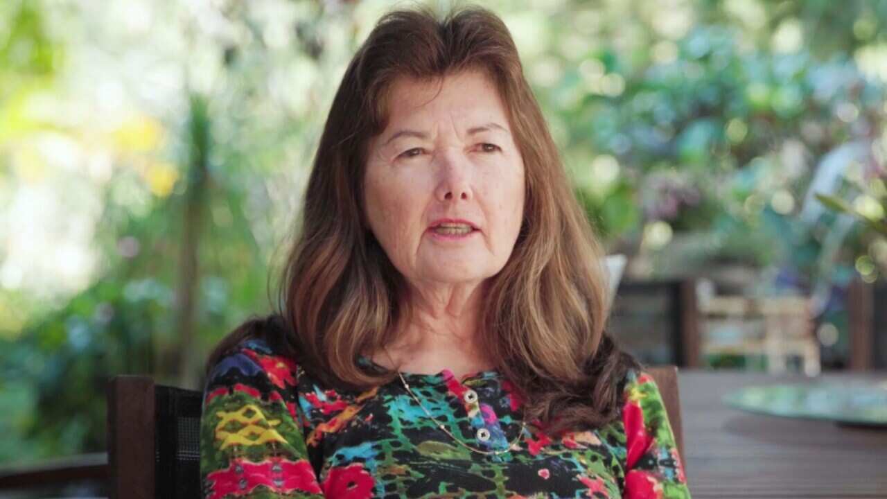 A woman speaking while seated on a chair outside.