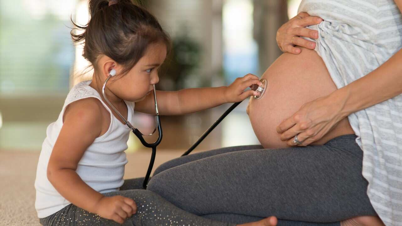 Cute toddler listening to her pregnant mother's belly