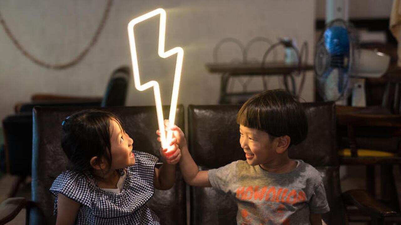 Two small children holding a lightning bolt shaped neon light