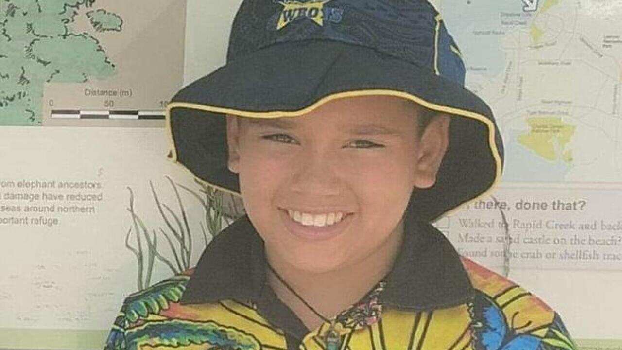 A boy poses in front of an information stand. He is wearing a NAIDOC shirt and a North Queensland Cowboys hat.