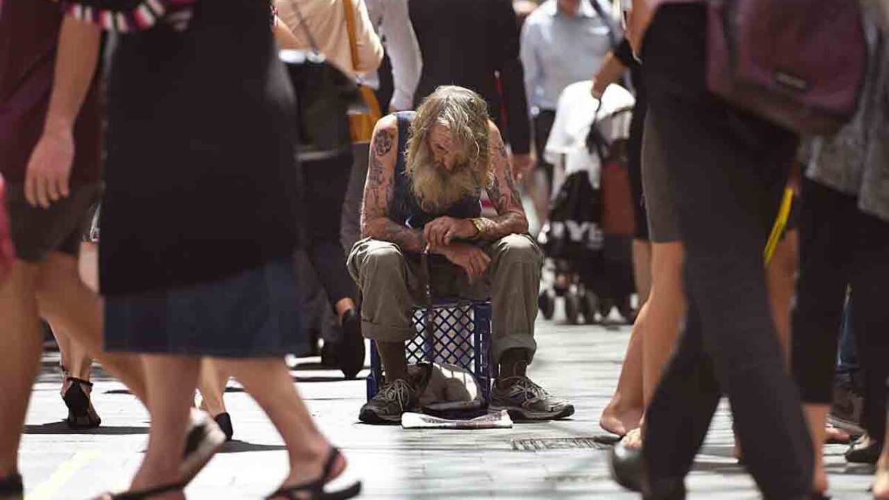 A homeless man sits on a milk crate on the street