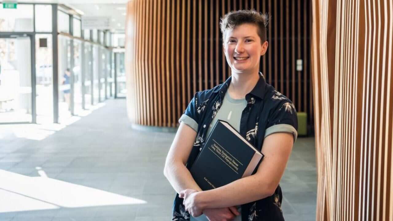 Ruth Monk standing and smiling and holding a book.