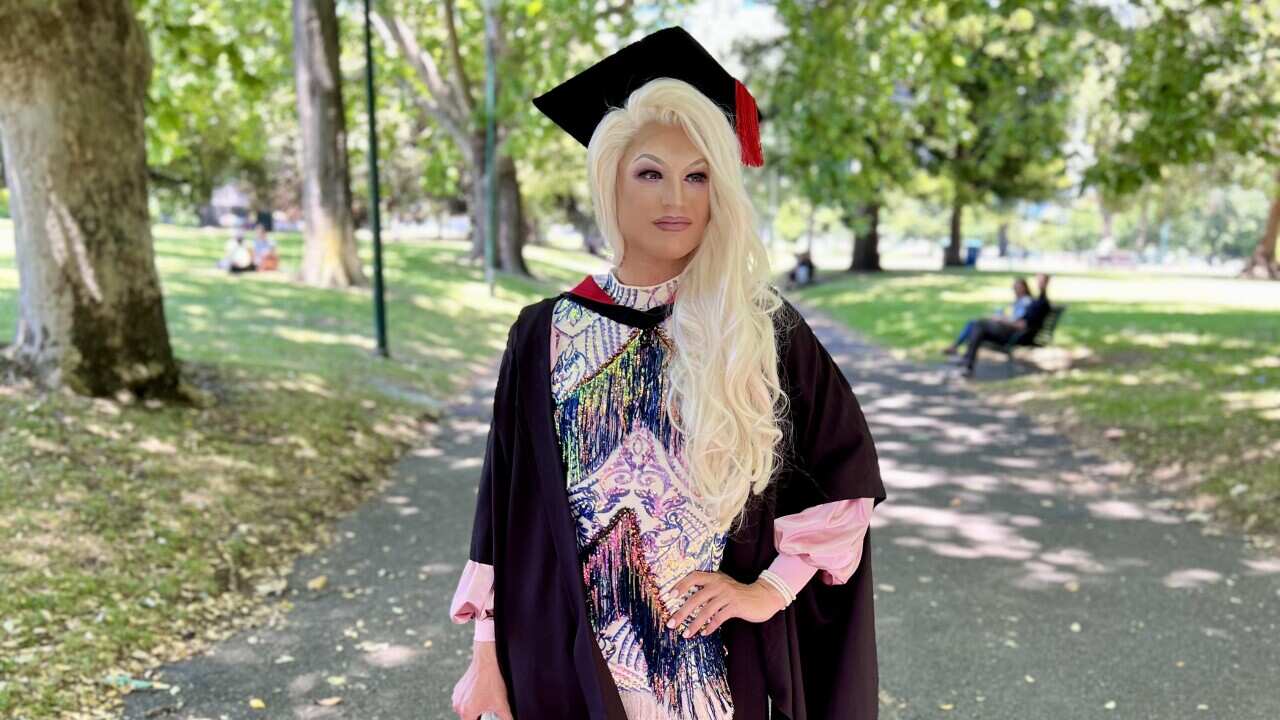 A person wears a sleeved dress with a blonde wig and high heels at their university graduation. 