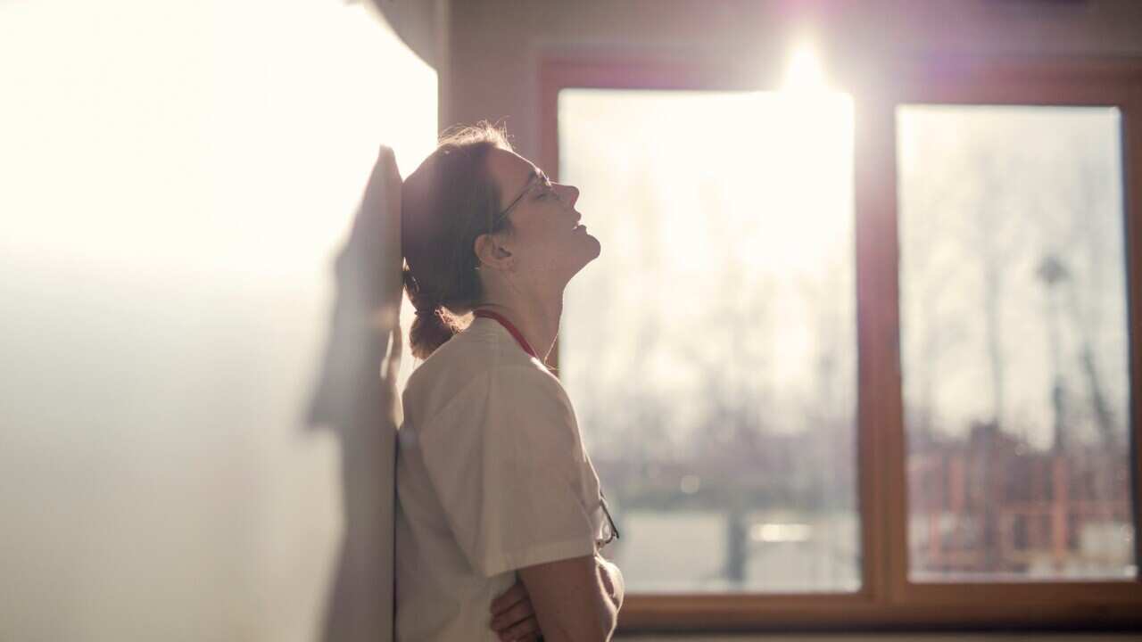Exhausted health care worker leans against a wall