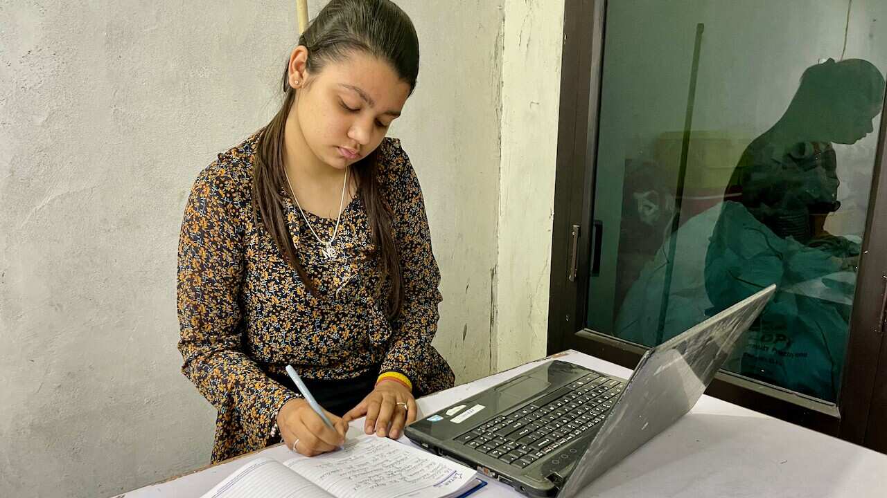 A woman writes in a notebook next to an open laptop