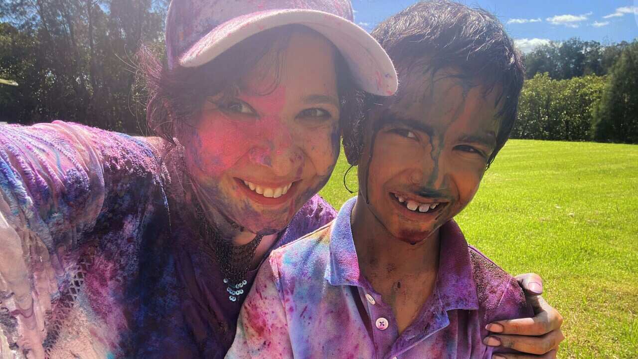 South Asian mother and son covered in colourful powder smiling at camera