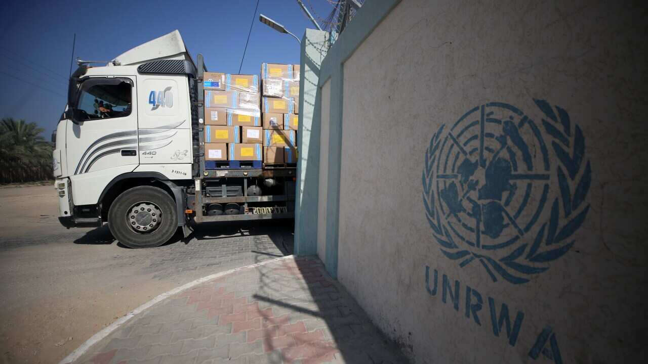 A truck with aid parcels driving past a wall with a UNRWA symbol on it.
