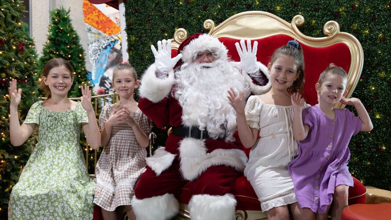 A man dressed in a Santa costume with two girls sitting either side of him