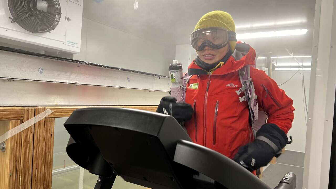 A woman runs on a treadmill inside a giant fridge, with cold mist surrounding her.