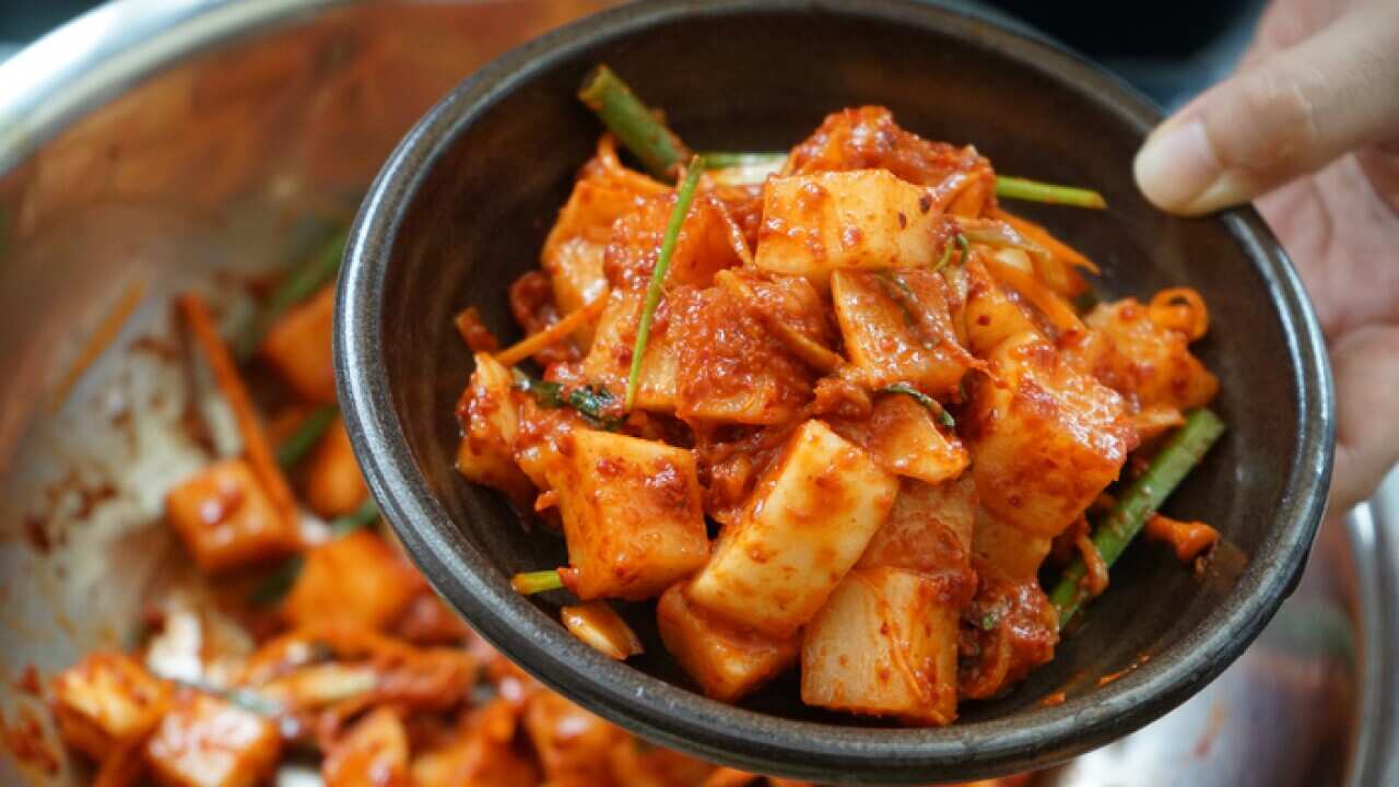 Cropped Image Of Hand Holding Kimchee In Bowl Over Cooking Pan