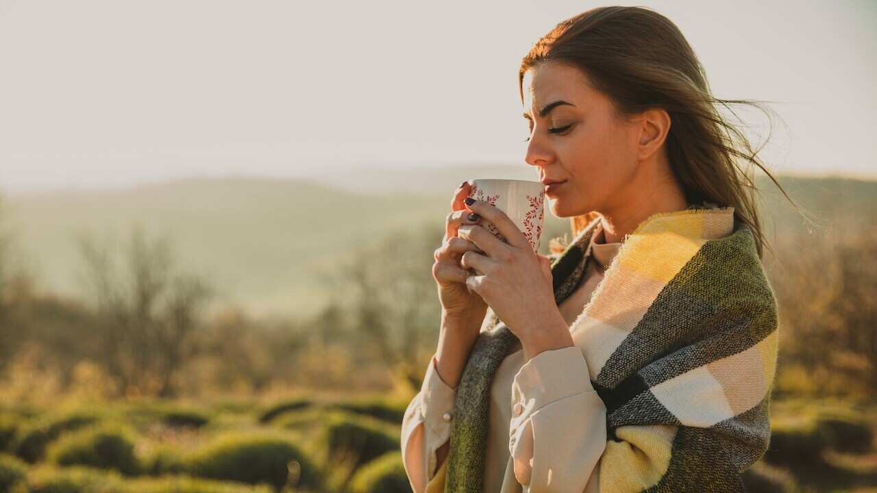 Beautiful woman enjoying warm autumnal sunshine and sipping tea while wrapped in a cozy scarf