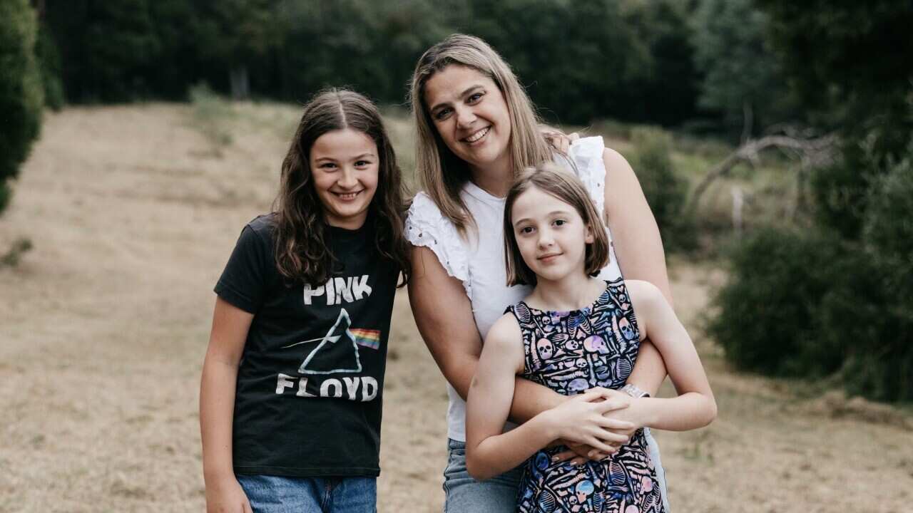 A mother and her two daughters stand together for a family photo. They are all smiling.