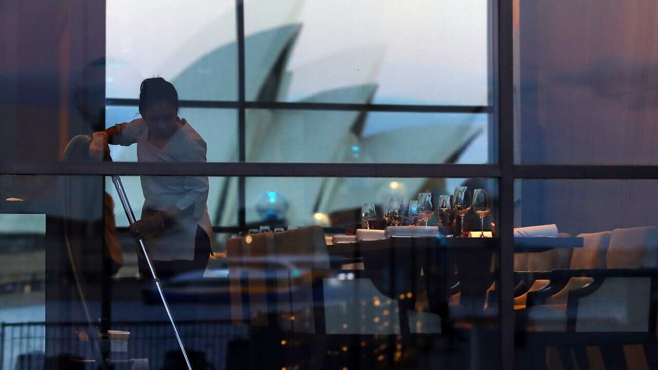 The Sydney Opera House can be seen in the reflection of a restaurant window as a worker uses a vacuum in Sydney