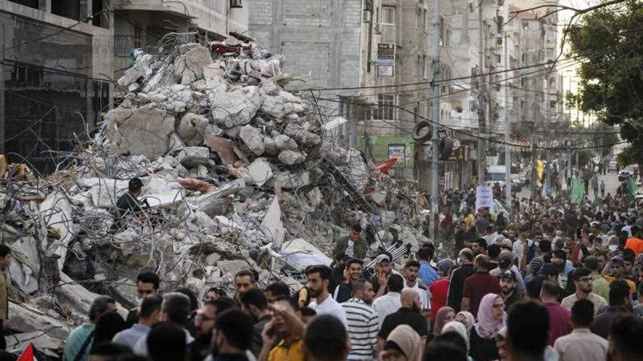 People pass a rubble heap beside a building previously destroyed by an air-strike following a ceasefire, 21 May 2021. 