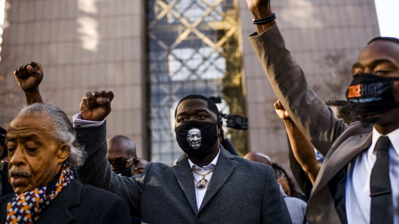 Brandon Williams wears a mask and pendant with the image of his uncle, George Floyd, and raises his fist at the courthouse in Minneapolis, Minnesota.