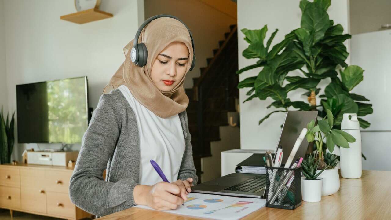 Muslim woman working on laptop computer in living room at home.