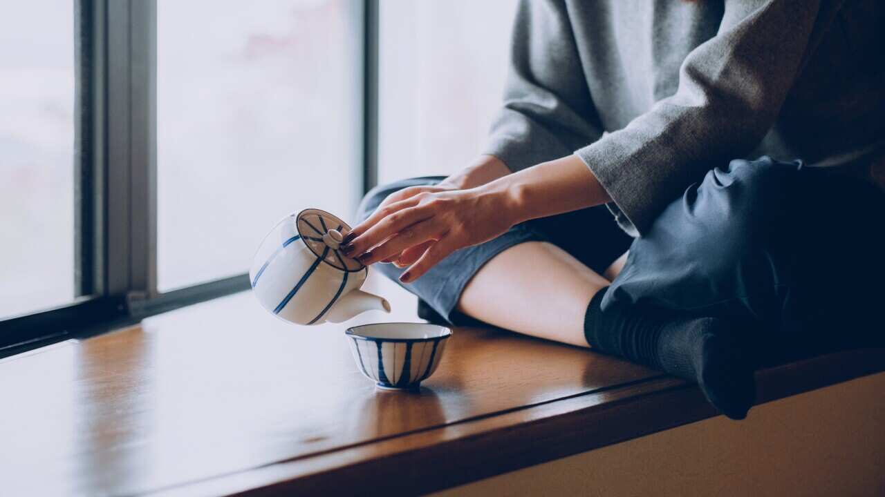 Woman sitting on the windowsill and pouring a cup of tea