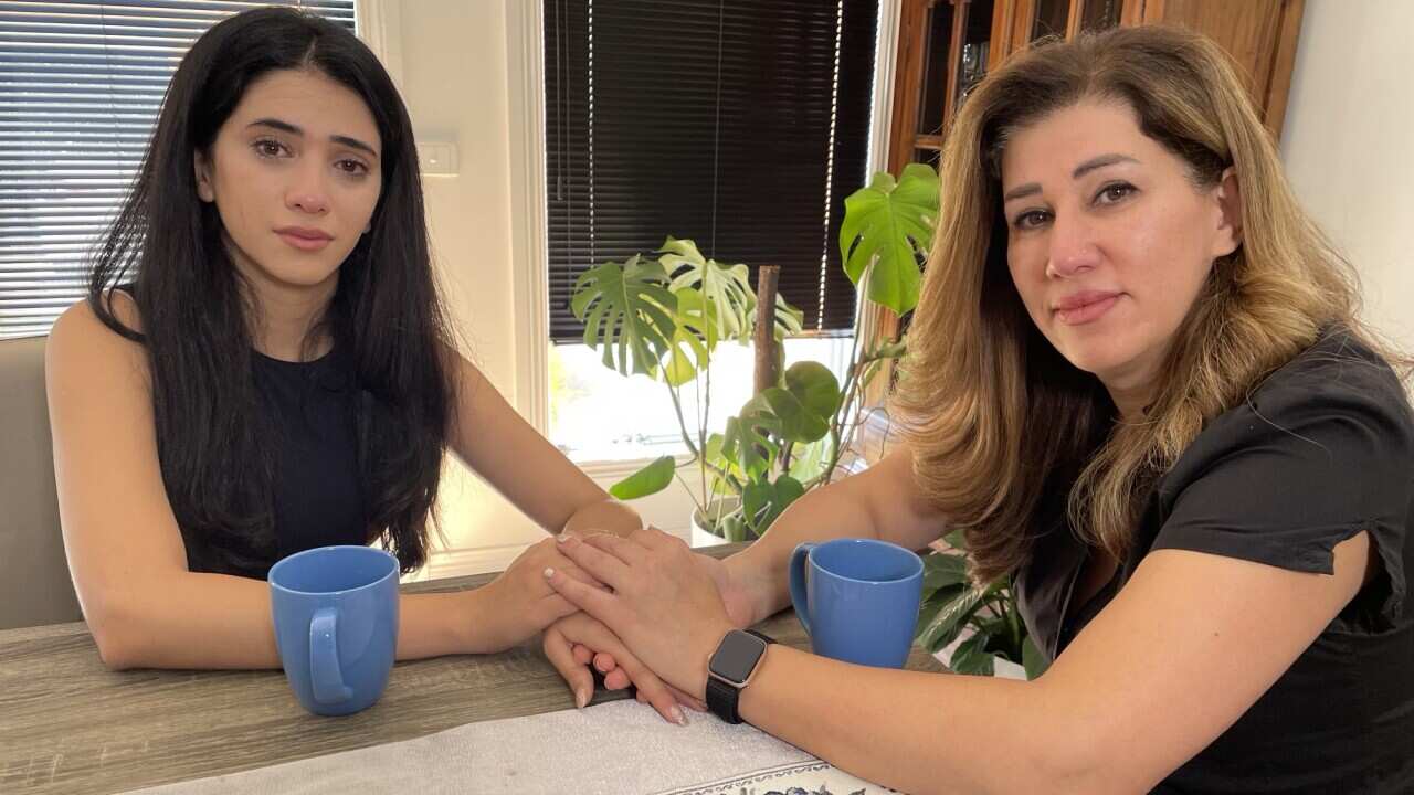 A mother and daughter hold hands while sitting at a table. 