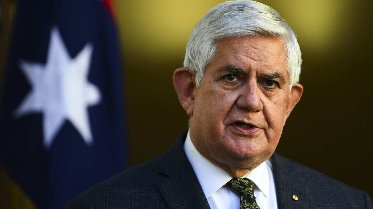 Man in tie speaking in front of Australian flag.