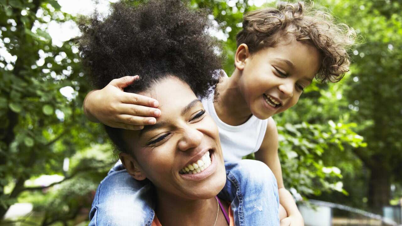 Mother with son on her shoulders in a park.