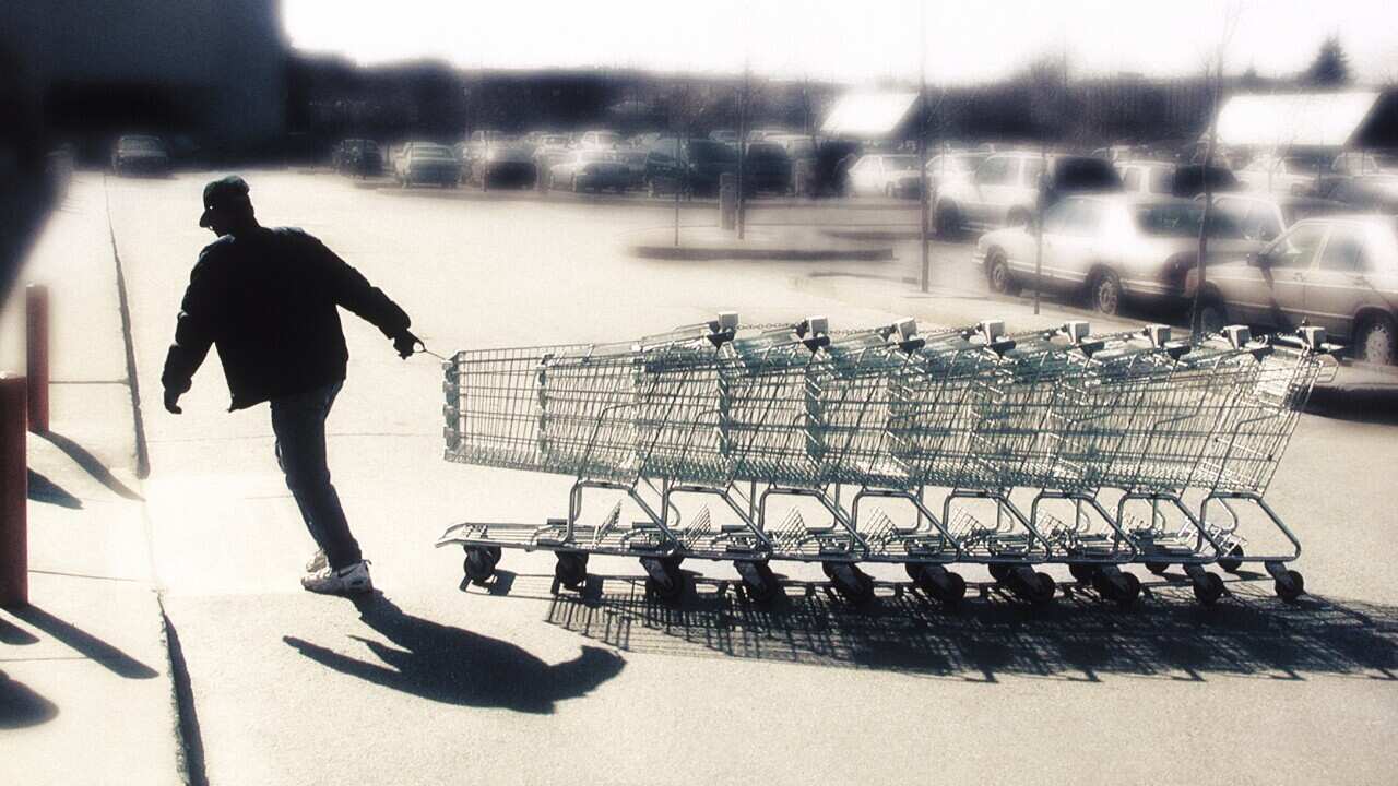 Man pulling a row of shopping trolleys through a carpark.