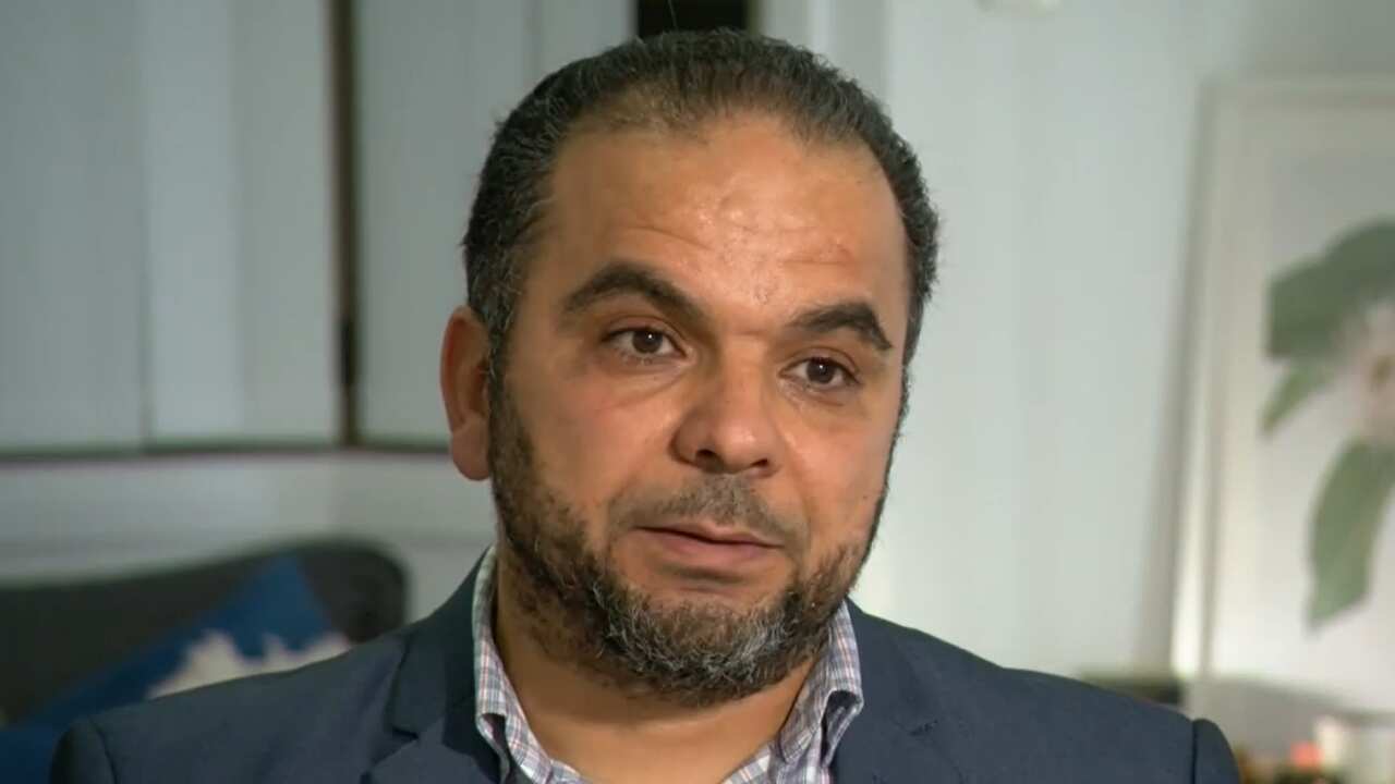 A man in a blue blazer and blue and white checked shirt