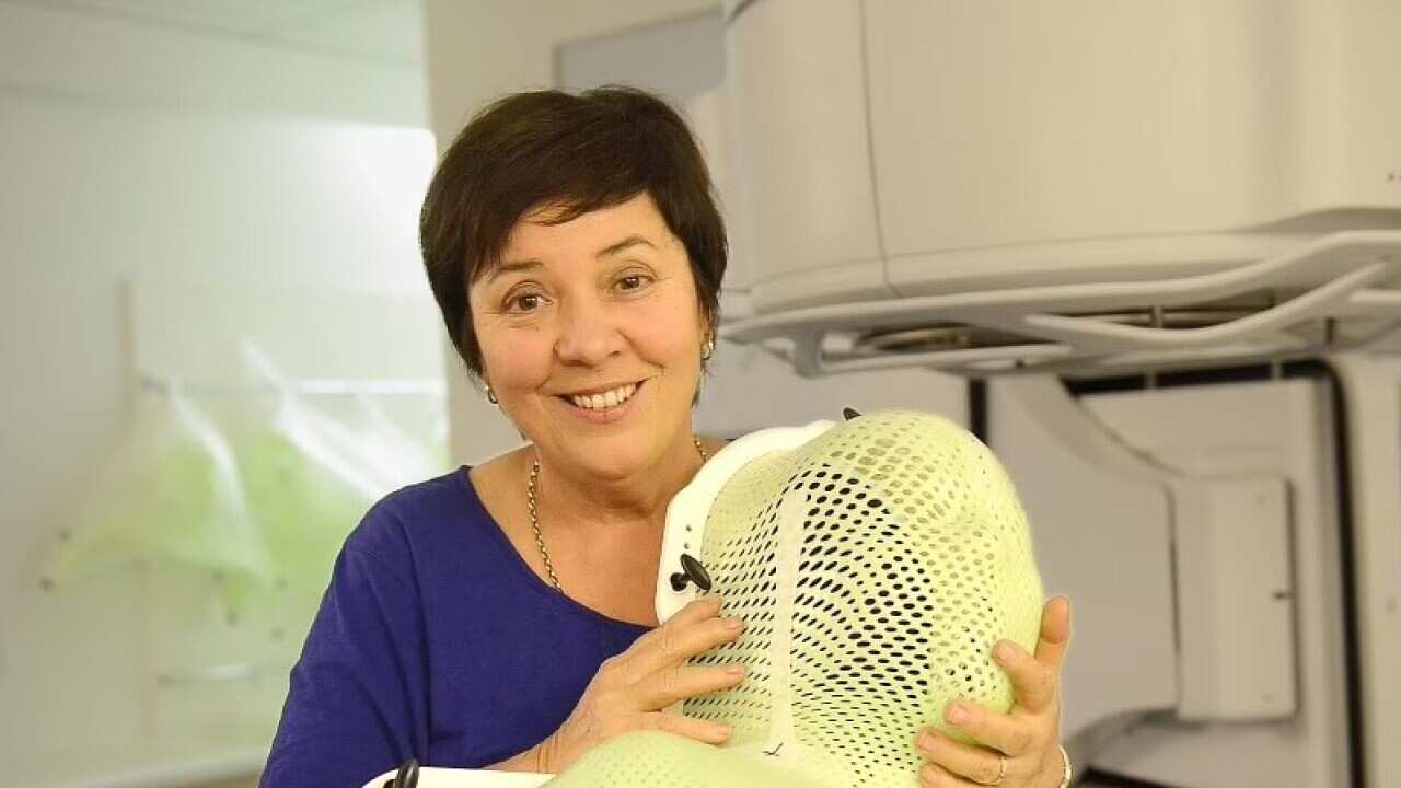 Julie McCrossin smiling in front of an MRI machine