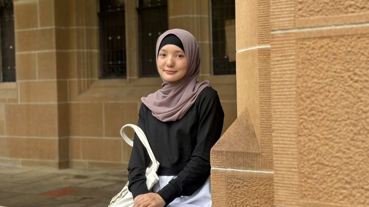 A young Muslim girl wearing a headscarf site next to a sandstone column.