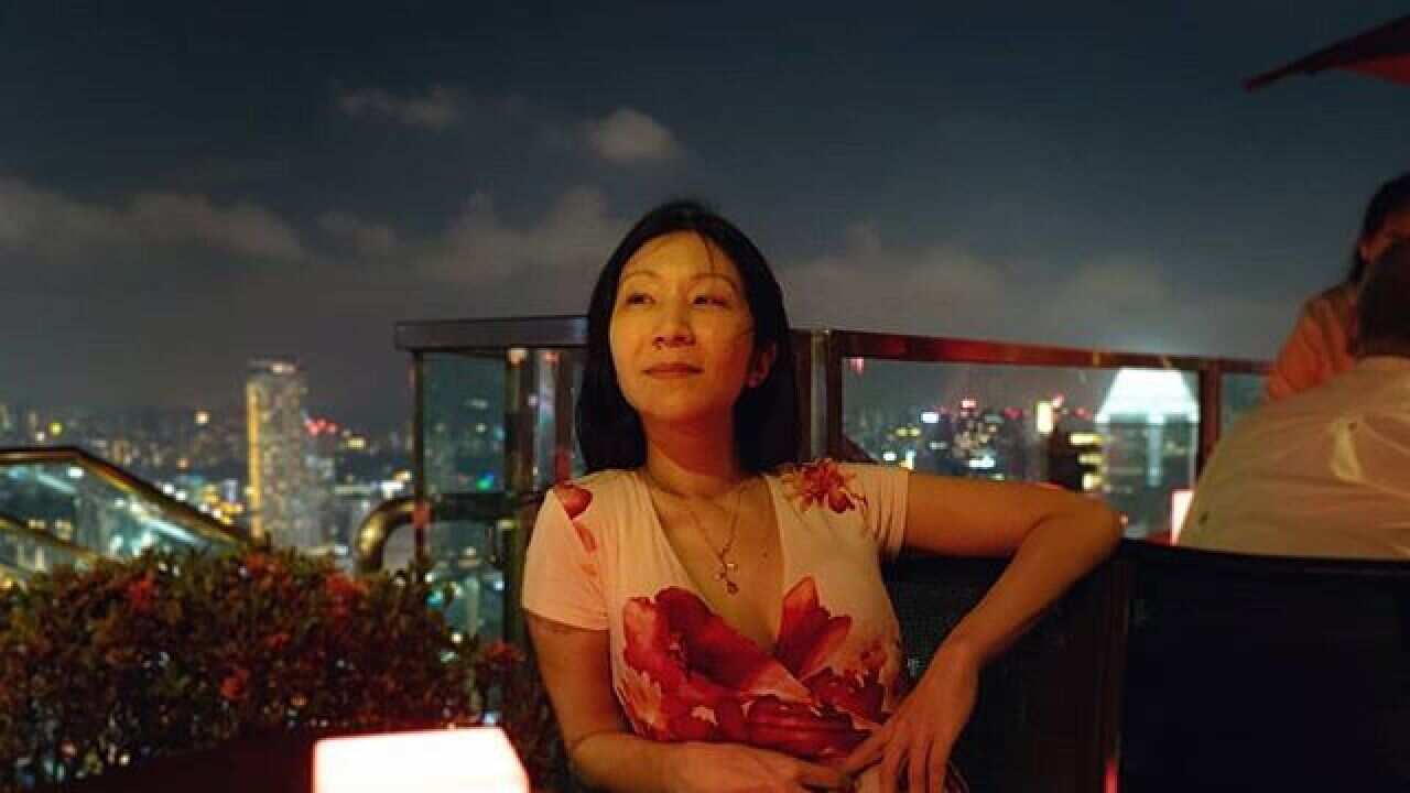 A woman looks ahead while seated and resting her arm on a table.