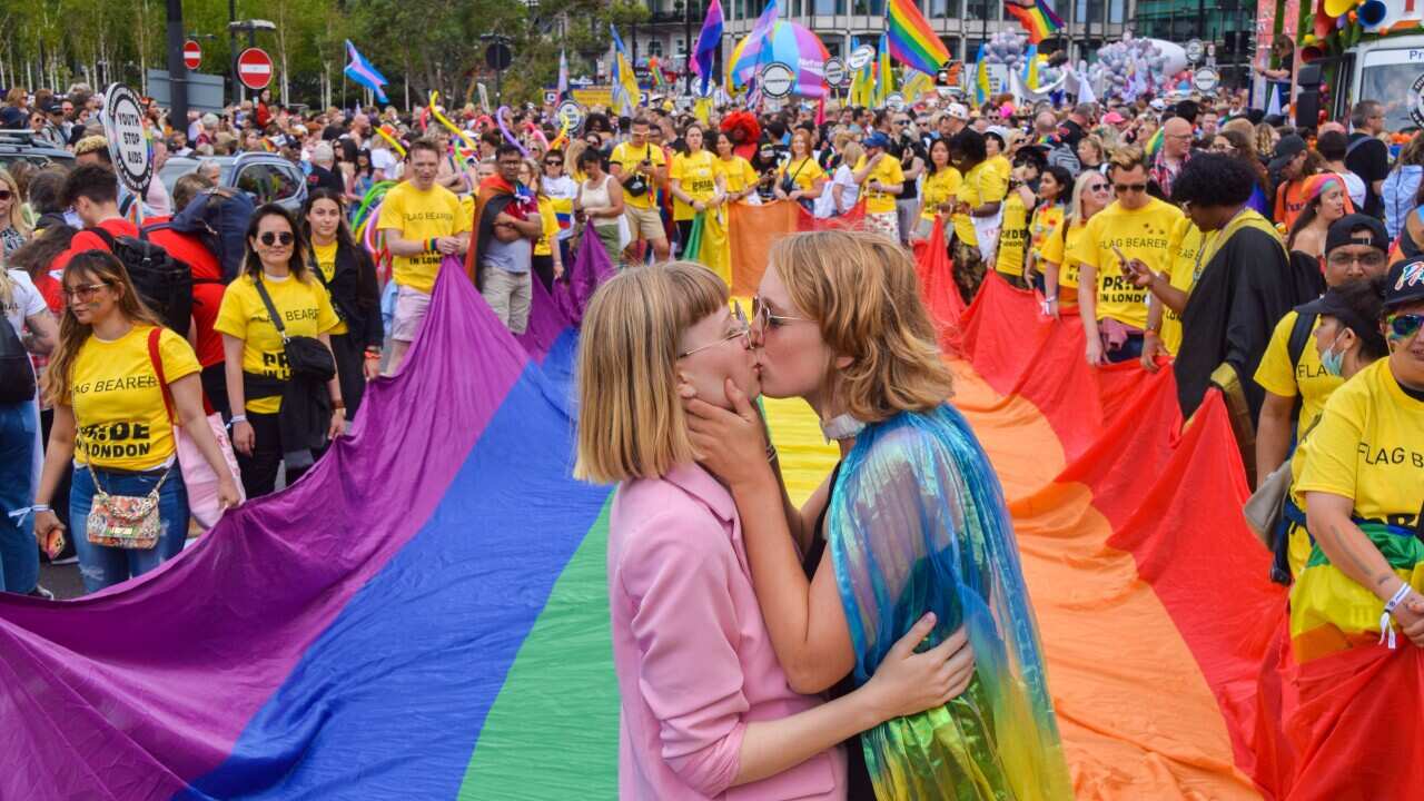 Two women kiss in front of a rainbow flag during a pride parade in London