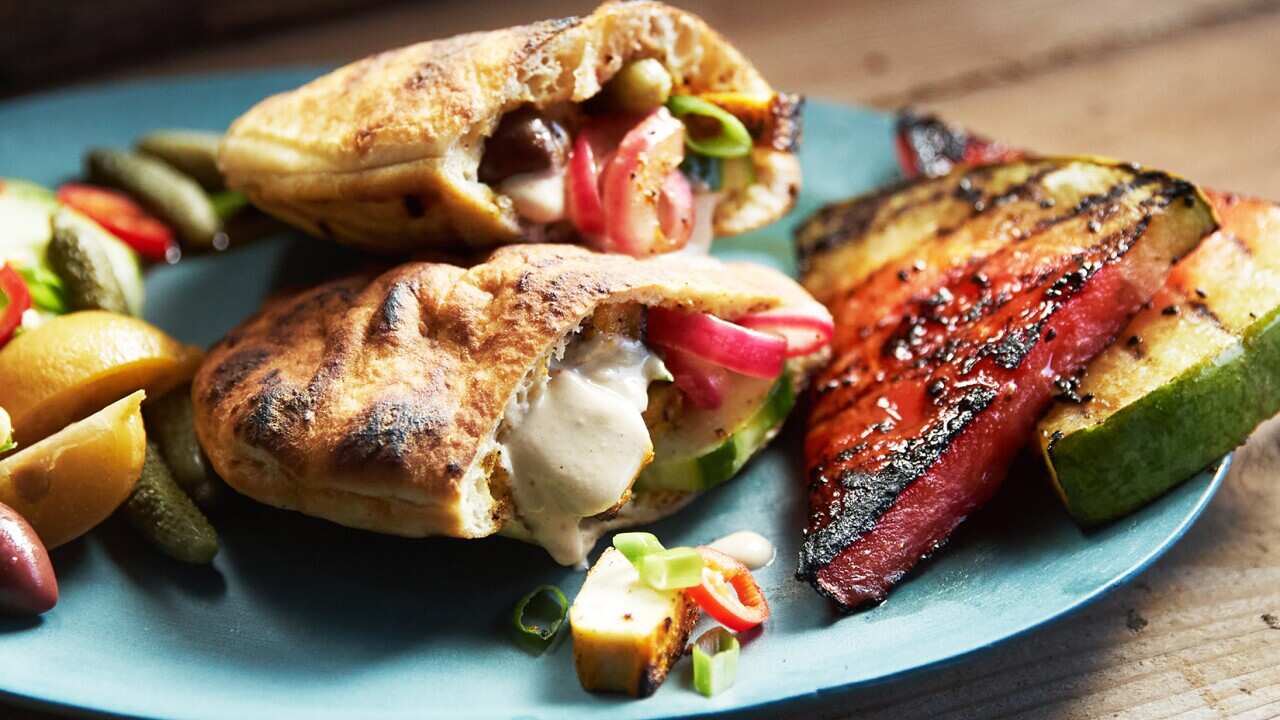 Two filled pitas sit on a round blue plate, alonside wedges of watermelon with char marks. 