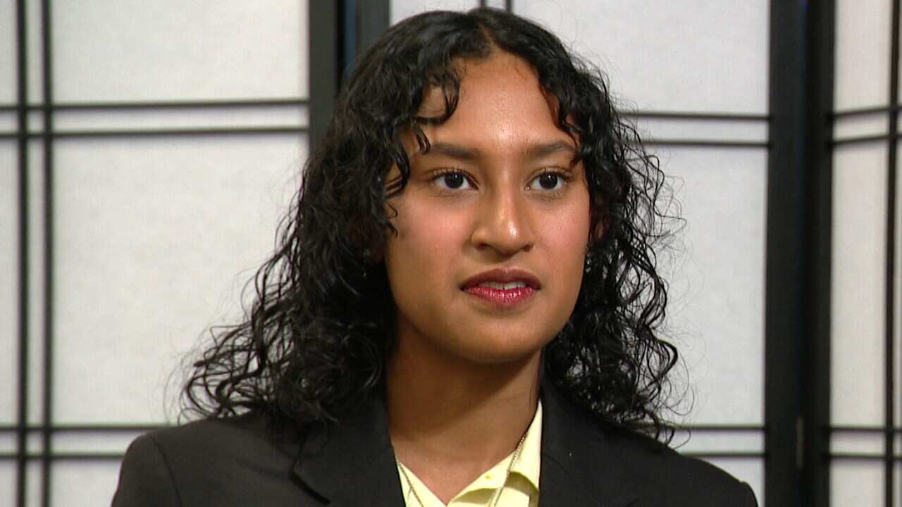 A woman wearing a high school blazer speaking to a journalist. 