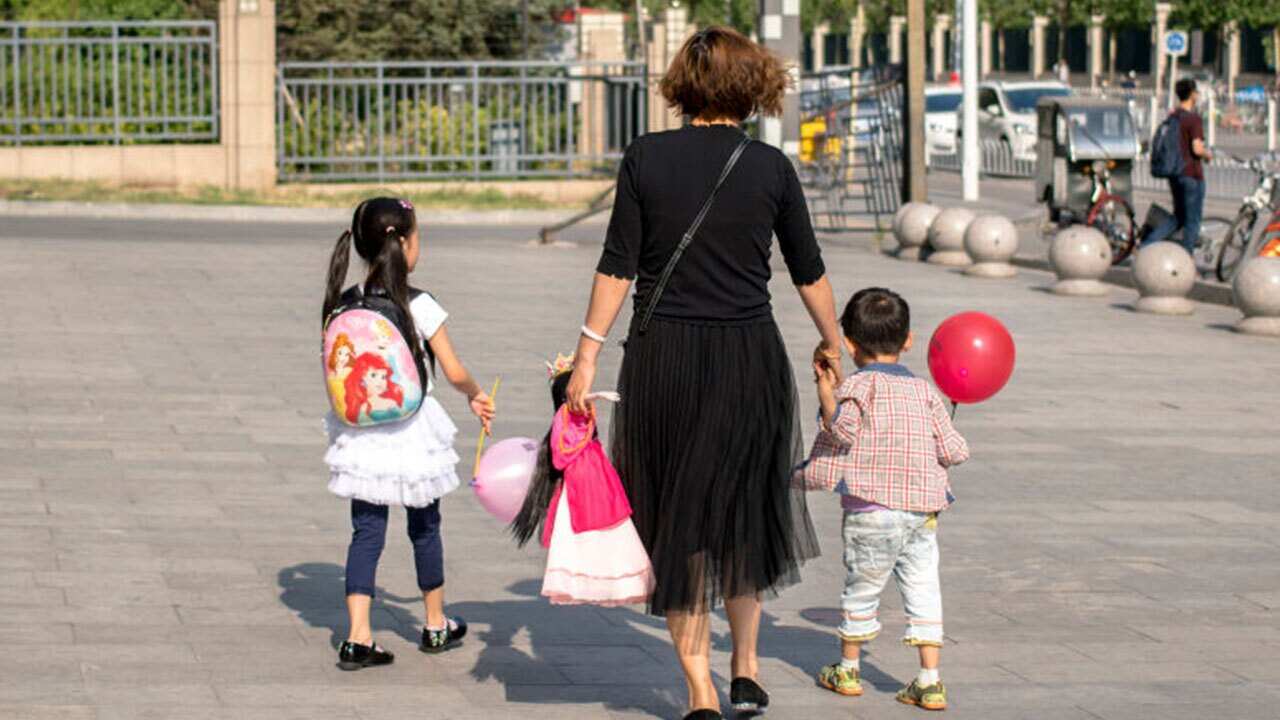 A mother takes her two kids walking on the street.