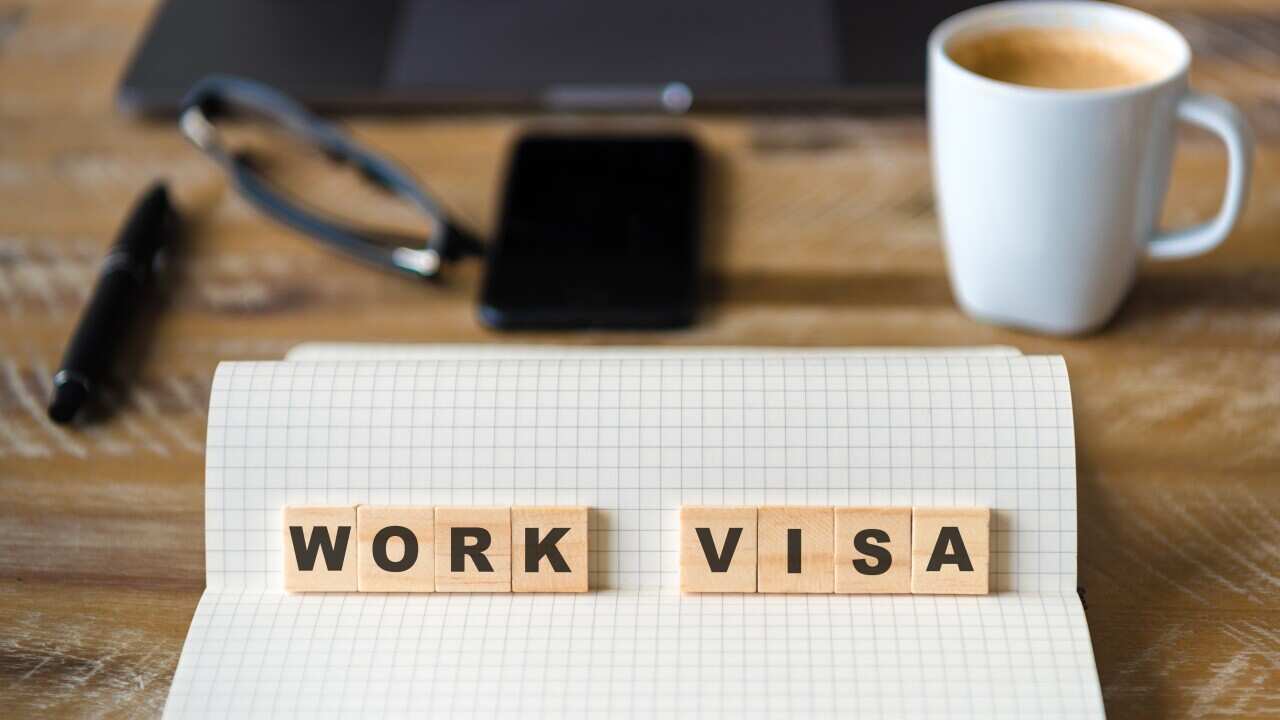 Closeup on notebook over wood table background, focus on wooden blocks with letters making Work Visa text