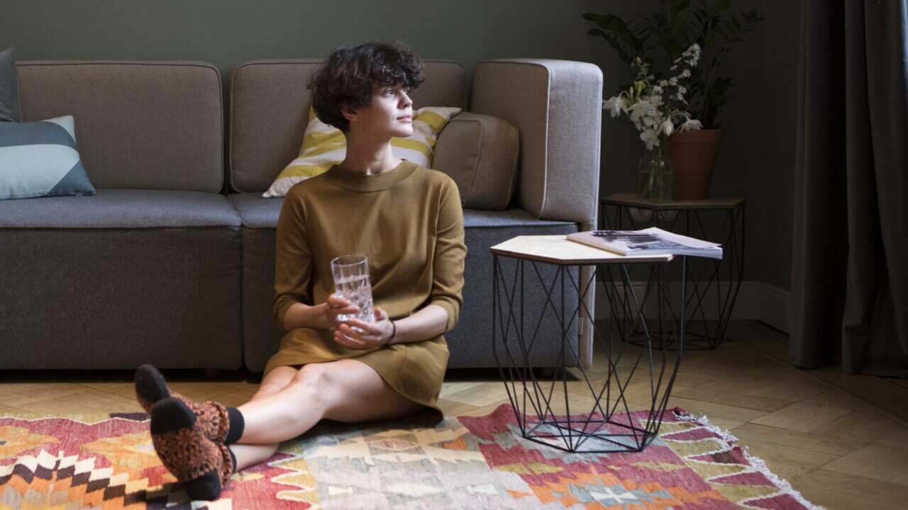 Young woman sitting on the floor in her living room looking through window