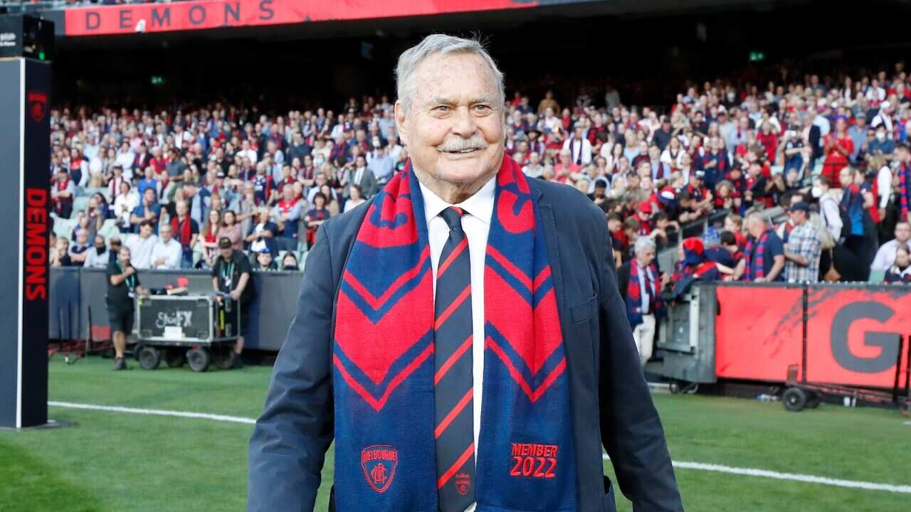 Ron Barassi in a blue and red scarf on a football field.