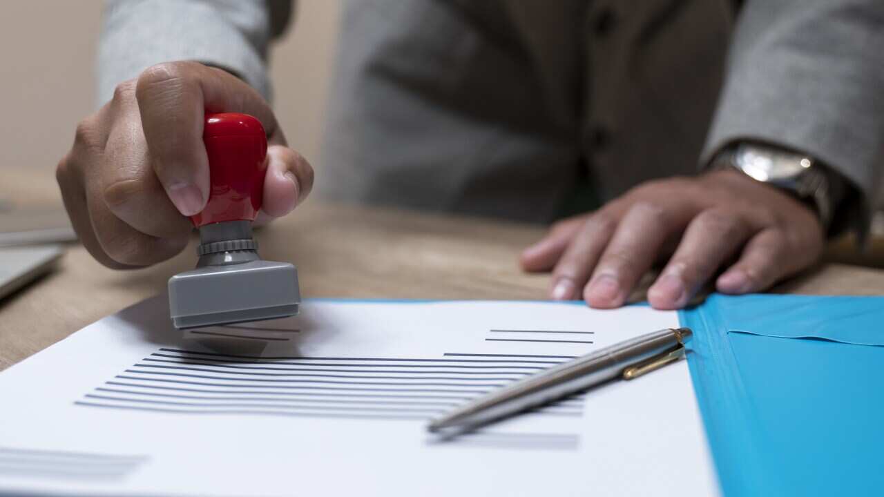 Close-up Of A Person's Hand Stamping With Approved Stamp On Document At Desk