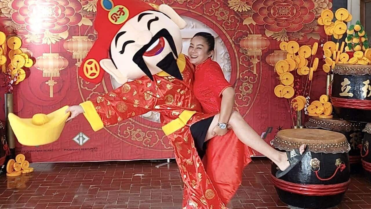 A woman wearing a red dress dancing with a person wearing a large papier-mache head featuring a red cap, droopy black moustache and pointy black goatee