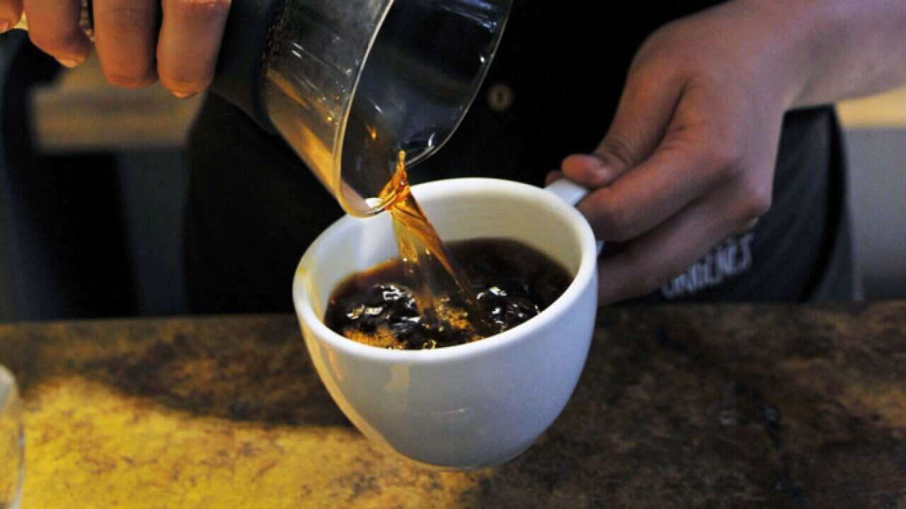 Barista pouring black coffee into cup