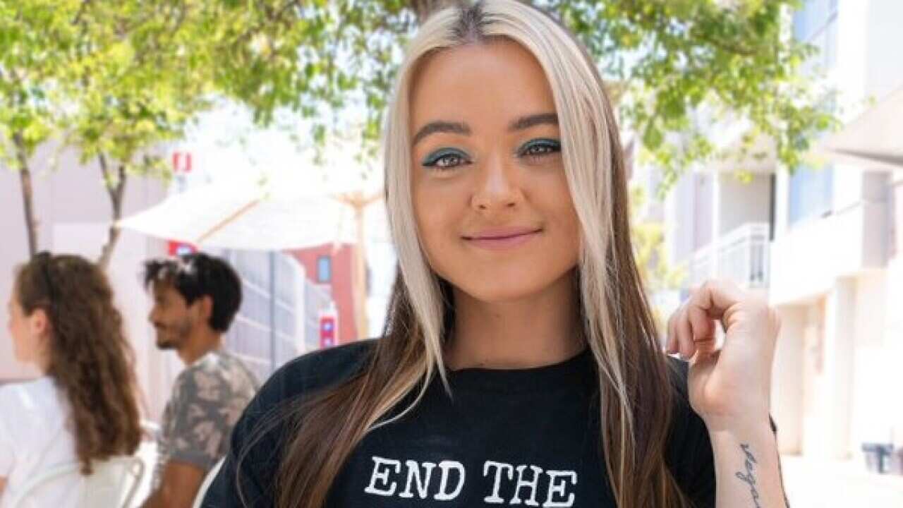 A woman sits smiling in front of a plate of vegan food, with her T-shirt reading "End the animal Holocaust".