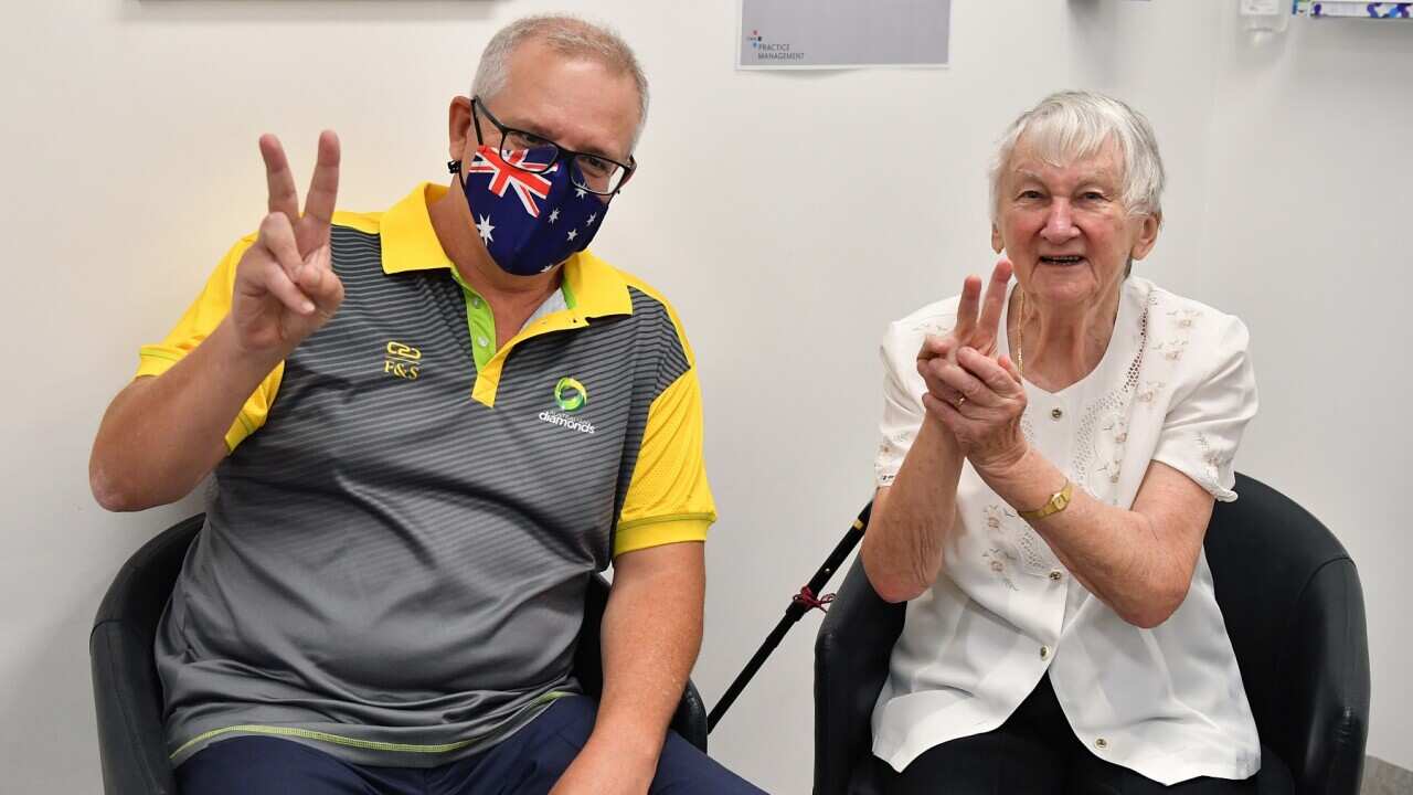 Australian Prime Minister Scott Morrison gestures alongside Aged care resident Jane Malysiak (left) as she receives her second COVID-19 vaccination.