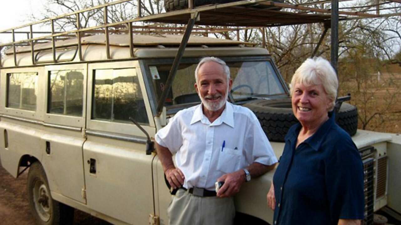 A man wearing a white shirt standing next to a woman wearing a dark top. Both are in front of a tan-coloured Land Rover vehicle