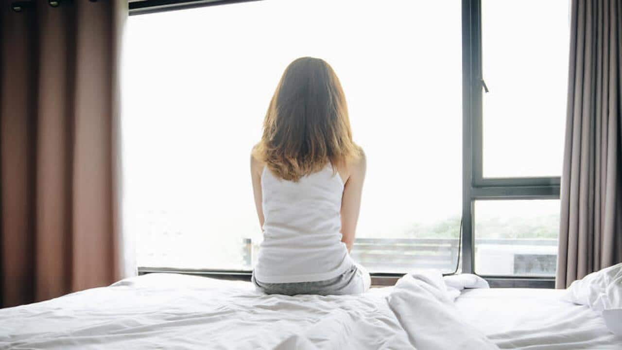 Portrait of depressed woman sitting alone on bed, looking to outside the window.