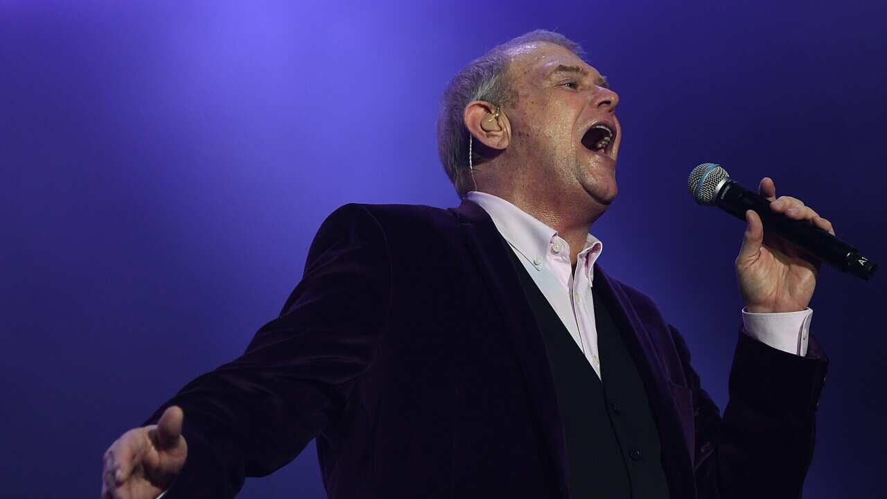 A man in a black suit sings with a microphone in his hand.